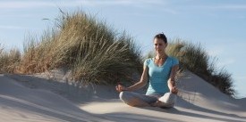 WHR – Achtsamkeit Wellness Hotels & Resorts: Junge Frau im Lotussitz in den Dünen